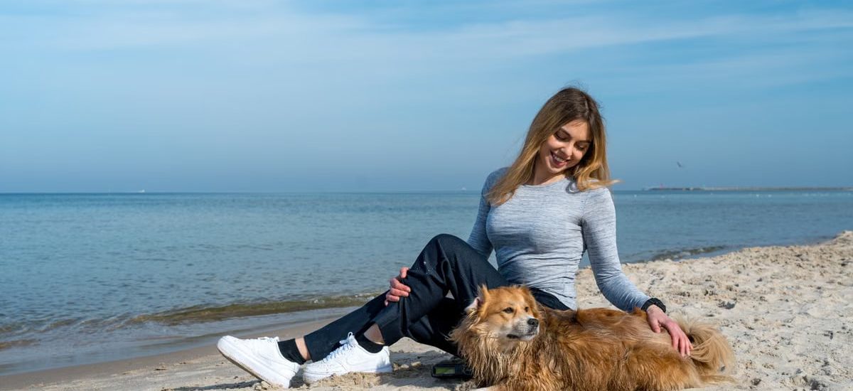 Woman enjoying a sunny day at Kołobrzeg beach with her dog, capturing a perfect seaside moment.