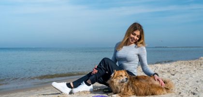 Woman enjoying a sunny day at Kołobrzeg beach with her dog, capturing a perfect seaside moment.
