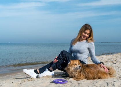 Woman enjoying a sunny day at Kołobrzeg beach with her dog, capturing a perfect seaside moment.